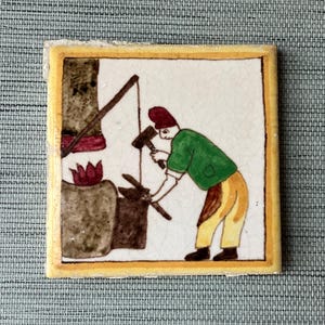 May include: A hand-painted ceramic tile depicting a person in a green shirt and yellow pants working at a forge. The tile has a yellow border and a white background.