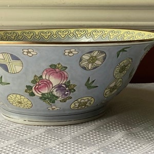 May include: A large, light blue porcelain bowl with a gold rim and intricate floral and geometric designs. The bowl is decorated with yellow, pink, green, and white flowers and patterns.