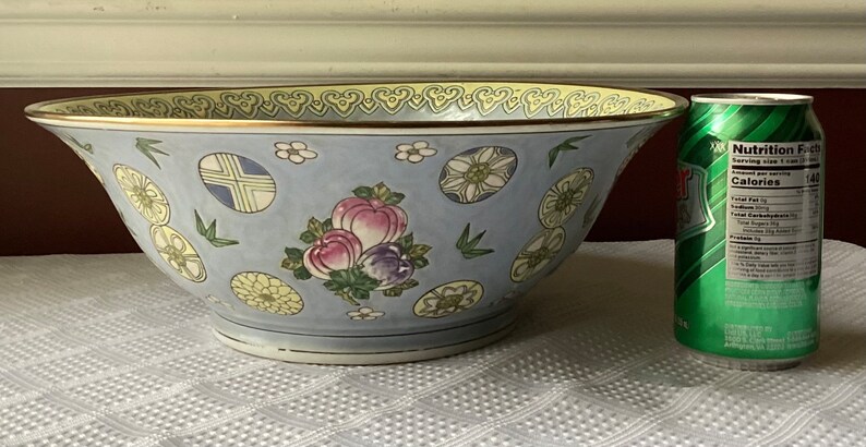 May include: A large, light blue porcelain bowl with a gold rim and intricate floral and geometric designs. The bowl is decorated with yellow, pink, green, and white flowers and patterns.