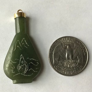 May include: A small green jade bottle pendant with a gold cap. The bottle is carved with a mountain scene and a bird in flight. The pendant is about the size of a US quarter.