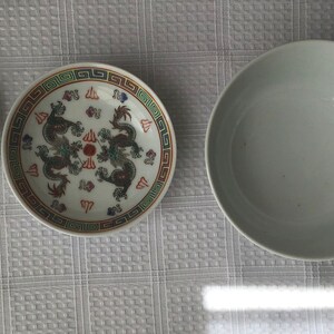 May include: A white ceramic bowl with a simple design, a white ceramic plate with a colorful dragon design, and a white ceramic spoon with a colorful dragon design.