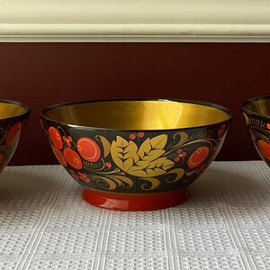 May include: Three black wooden bowls with gold rims and red and gold floral designs. The bowls are painted in a traditional Russian folk art style.