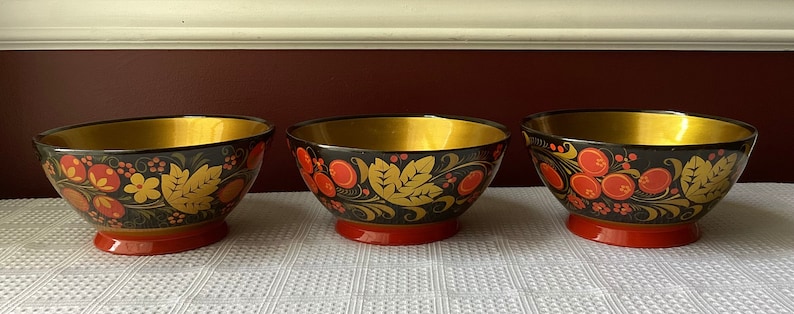 May include: Three black wooden bowls with gold rims and red and gold floral designs. The bowls are painted in a traditional Russian folk art style.