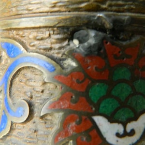K&ouml;nnte beinhalten: Nahaufnahme eines dekorativen Objekts aus Silber und Emaille mit einem floralen Design. Das Design zeigt eine rote Blume mit gr&uuml;nen Bl&auml;ttern und blauen Akzenten.