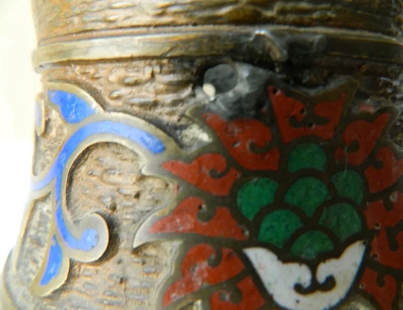 K&ouml;nnte beinhalten: Nahaufnahme eines dekorativen Objekts aus Silber und Emaille mit einem floralen Design. Das Design zeigt eine rote Blume mit gr&uuml;nen Bl&auml;ttern und blauen Akzenten.