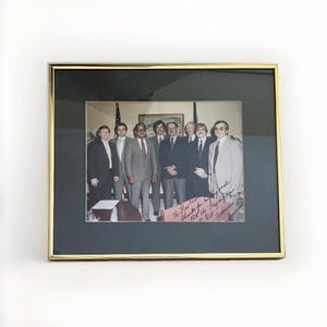May include: A framed black and white photograph of a group of men in suits standing in a room. The men are smiling and looking at the camera. The photo is signed by the men. "To How the - Thanks for the help -  Nick the Frog -  At H.S.K. -  Appreciation"