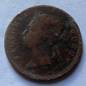 May include: A worn, copper-colored coin featuring a profile of a person and the inscription "VICTORIA QUEEN". The coin's surface shows signs of age and wear, with visible scratches and discoloration. The coin's design includes text around the edge.
