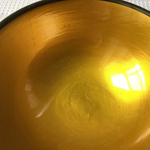 May include: A large, round, golden bowl with a black rim. The bowl is made of a smooth, shiny material and has a slight reflection of light.