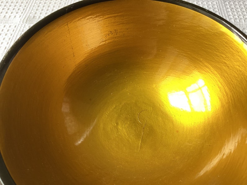 May include: A large, round, golden bowl with a black rim. The bowl is made of a smooth, shiny material and has a slight reflection of light.