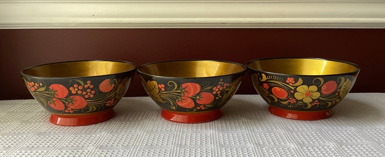 May include: Three black and gold bowls with red and gold floral designs. The bowls are made of wood and have a glossy finish.