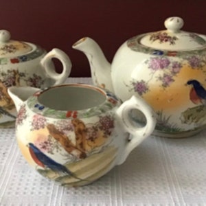 May include: A white porcelain tea set with a floral and bird design. The set includes a teapot, creamer, and sugar bowl.