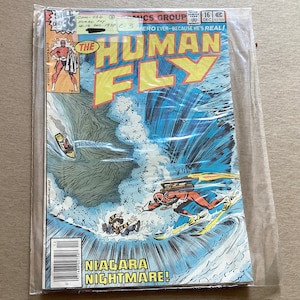May include: A comic book cover featuring a superhero in a red and yellow suit flying through a large wave. The title of the comic is "The Human Fly" and the tagline is "Hero Ever--Because He's Real!" The cover also features the text "Niagara Nightmare!"