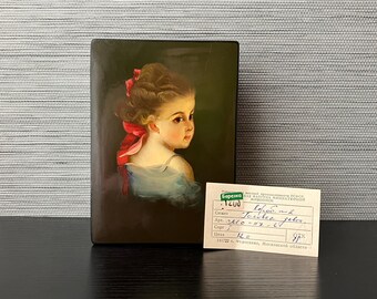 May include: A small wooden box with a painted portrait of a young girl with a red ribbon in her hair. The box has a label with the text "Сюжет  Березка РНКА МИНИАТЮРНОЙ живописи  Torster tea geler.  Coge  leva 12= 97 141722 6. Федоскино, Московской области".