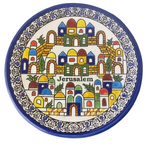 May include: A round ceramic plate with a blue rim and a detailed illustration of Jerusalem. The image features colorful buildings, arches, and the word "Jerusalem". The plate has a decorative border with floral patterns.