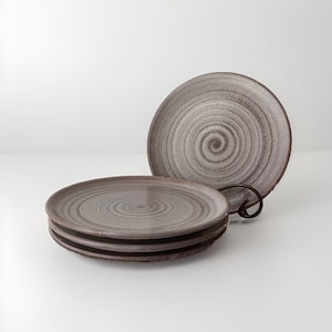 May include: Set of four ceramic plates with a swirling grey and white glaze. The plates are stacked on top of each other.