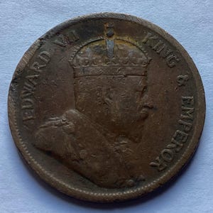 May include: A copper-colored coin featuring a profile of a crowned figure, with the inscriptions "EDWARD VII KING & EMPEROR" around the edge. The coin shows signs of wear and age, with a slightly irregular shape.