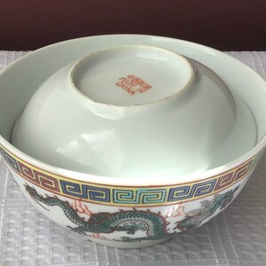 May include: A white porcelain bowl with a dragon design and a yellow, red, and blue border. The bowl is made in China and has the text "Made in China" on the bottom.