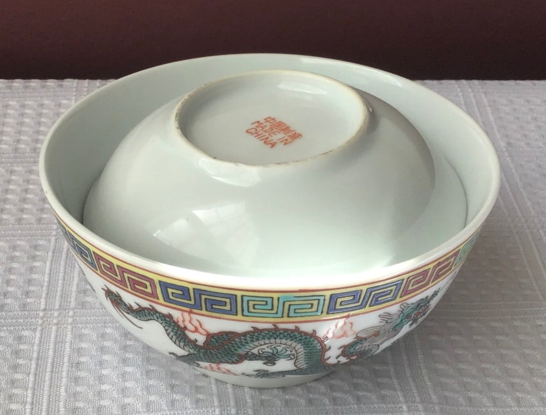 May include: A white porcelain bowl with a dragon design and a yellow, red, and blue border. The bowl is made in China and has the text "Made in China" on the bottom.