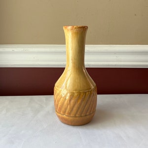May include: A yellow ceramic vase with a brown swirl design. The vase has a narrow neck and a rounded body.