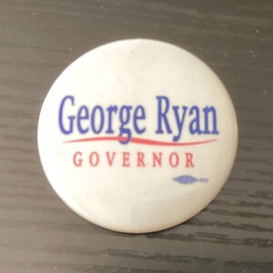 May include: A white campaign button with the text "George Ryan" in blue, above the word "GOVERNOR" in red. A red line underlines the name. A small blue design is at the bottom.