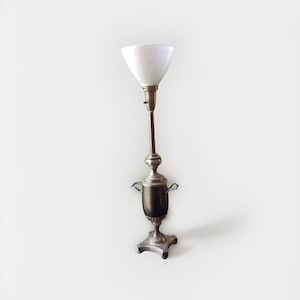 May include: An antique floor lamp with a white, cone-shaped shade. The lamp has a dark brown base with silver accents and a long, slender stem. The lamp's design is reminiscent of vintage decor.