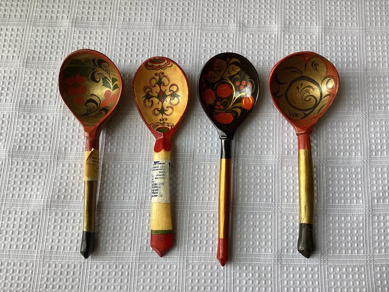 May include: Four wooden spoons with hand-painted designs. The spoons are red, yellow, and black with floral and geometric patterns.