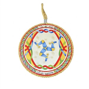 May include: A circular hanging ornament featuring the Isle of Man triskelion symbol in blue and yellow. The border displays red, green, and blue Celtic knotwork with the text "isle of man" and "ellan vannin" and a gold twisted rope trim.