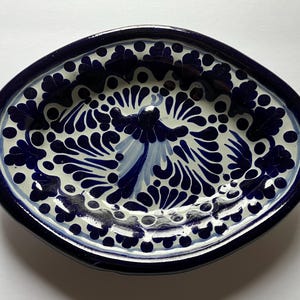May include: Oval ceramic serving dish with a dark blue rim and intricate white and blue floral patterns. The dish features a central design and is suitable for serving food or as a decorative piece.