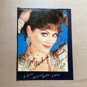 May include: A signed photograph of a woman with dark hair and a sparkling gold top. The signature reads "To Ms. Anni, Thank you very good friends, Cheers, Della."