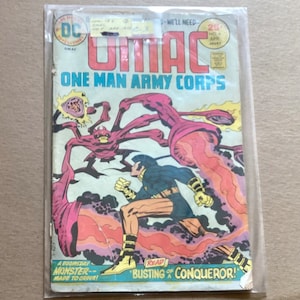 May include: A vintage comic book cover featuring a superhero called OMAC, the One Man Army Corps, battling a monstrous creature with glowing red eyes and tentacles. The cover is in a plastic sleeve.