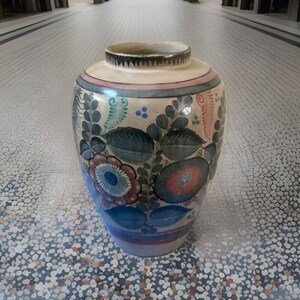 May include: A ceramic vase with a floral design in shades of blue, red, green, and white. The vase has a rounded body and a narrow neck.