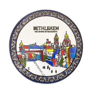 May include: A round, decorative plate featuring a colorful illustration of Bethlehem's Church of the Nativity. The plate has a blue border and a detailed, patterned edge. The text "BETHLEHEM THE CHURCH OF THE NATIVITY" is displayed at the top.