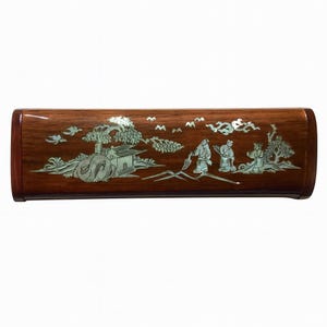 May include: A rectangular wooden box with a glossy finish. The box is adorned with a detailed mother-of-pearl inlay depicting a landscape with figures, trees, and a building. The wood has a rich, reddish-brown hue.