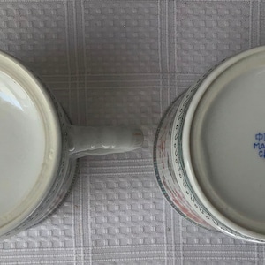 May include: Two white ceramic mugs with blue and red floral designs. The bottom of each mug reads "Made in China" in blue lettering.