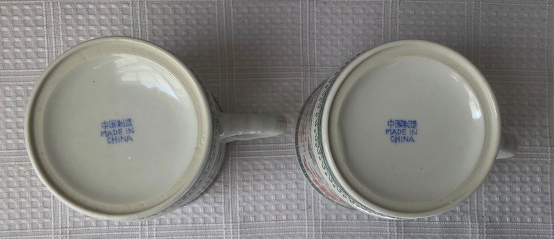 May include: Two white ceramic mugs with blue and red floral designs. The bottom of each mug reads "Made in China" in blue lettering.