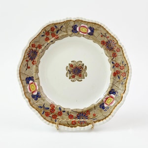 May include: A round ceramic plate with a scalloped edge featuring a central floral motif and a wide border decorated with a tan crackle pattern, red blossoms, blue star-shaped flowers, and pink-centered blooms with gold trim accents.