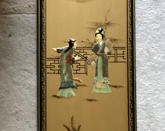 May include: A framed wall art piece with a gold background and a scene of two figures in traditional clothing standing in front of a wall. The figures are made of ivory and the background is painted with black ink. The frame is black with a gold trim.