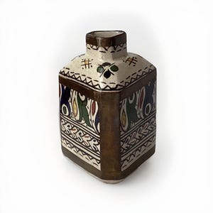 May include: A square ceramic vase with a white background and intricate geometric patterns in shades of green, blue, red, and yellow. The vase has a brown border and a slightly raised rim.