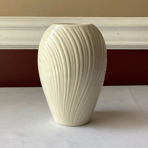 May include: A white ceramic vase with a ribbed design. The vase is oval shaped and has a smooth, glossy finish.