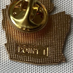 Op de afbeelding: Gouden metalen pin met een gedetailleerd ontwerp. De achterkant van de pin heeft de tekst "POINT II" gegraveerd.