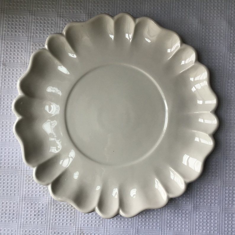 May include: A white ceramic plate with a scalloped edge. The plate is round and has a smooth, glossy finish.