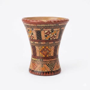 May include: A handcrafted, decorative vase with a wide top and a narrow base. The vase features intricate geometric patterns in shades of brown, orange, and black. The rim is painted red, and the interior appears to be natural wood.