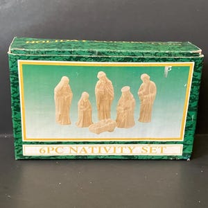 May include: A boxed 6-piece Nativity set. The box is green with a white border and the words "6PC NATIVITY SET". The set includes figures of Mary, Joseph, baby Jesus, and the three wise men. The figures are beige.