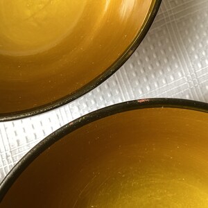 May include: Two yellow ceramic bowls with black rims. The bowls are empty and sitting on a white surface.