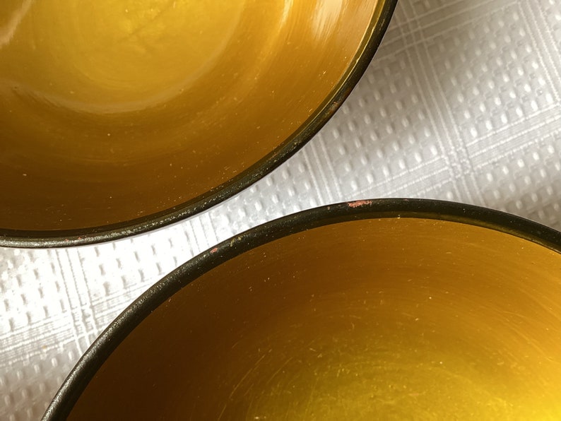 May include: Two yellow ceramic bowls with black rims. The bowls are empty and sitting on a white surface.