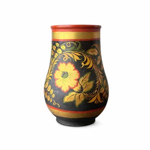 May include: A hand-painted, wooden vase with a black background and floral design. The vase features a large yellow flower and gold and green leaves. The rim is red with a gold band, and the base has a gold band.