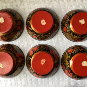 May include: Six black and red painted wooden bowls with gold accents and floral designs. The bowls are turned upside down, revealing the red interior.