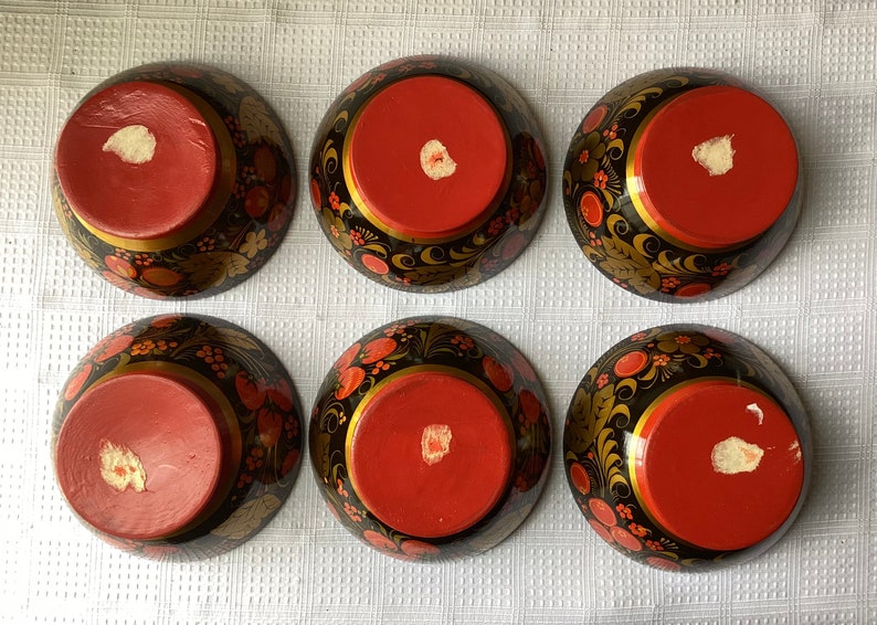May include: Six black and red painted wooden bowls with gold accents and floral designs. The bowls are turned upside down, revealing the red interior.