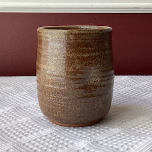 May include: A brown ceramic vase with a textured, speckled finish. The vase has a rounded shape and a slightly flared lip.