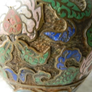K&ouml;nnte beinhalten: Eine runde, braune Keramikvase mit floralem Design. Die Vase ist mit gr&uuml;nem, blauem und rosa Email verziert. Die Vase hat eine strukturierte Oberfl&auml;che.
